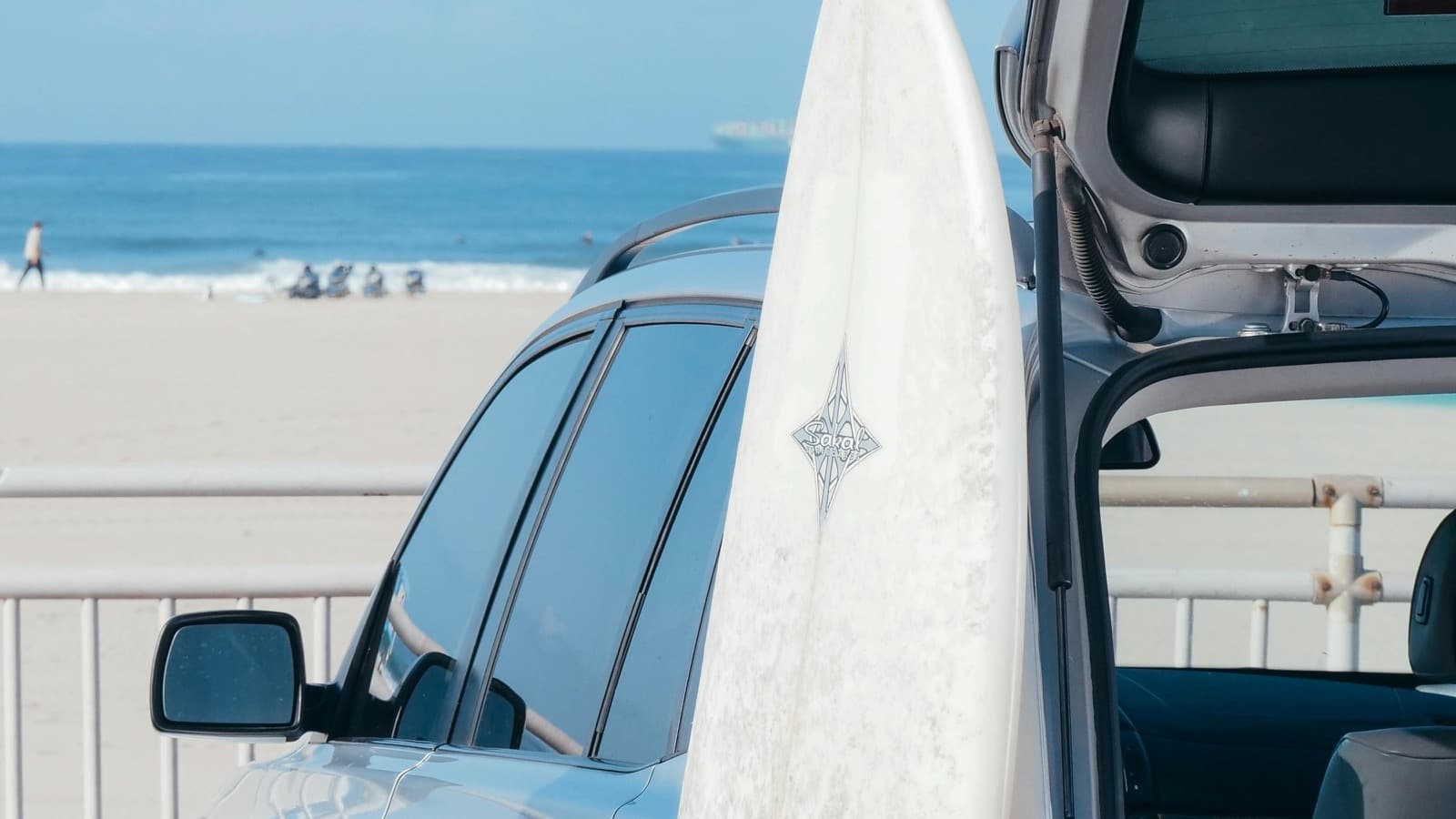 SUV parked near the beach with an open cargo area and a surfboard