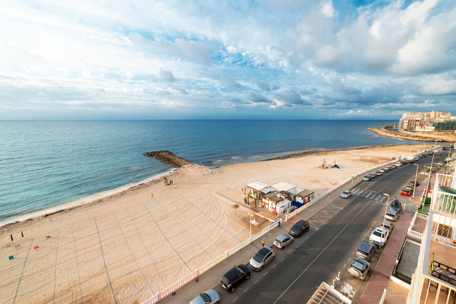 Cars parked along a beach road beside calm ocean water